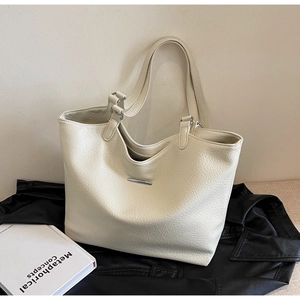 Macro detail of creamy pebble leather tote bag with silver hardware on black leather jacket