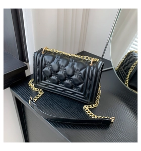 Detail of black quilted handbag with textured floral pattern and gold chain strap