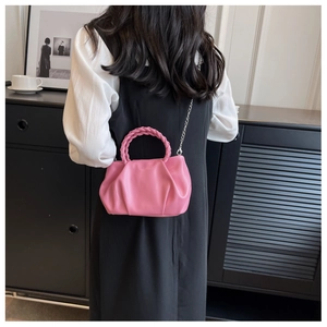 Pink pleated cloud bag with woven handle and metallic chain strap on model shoulder