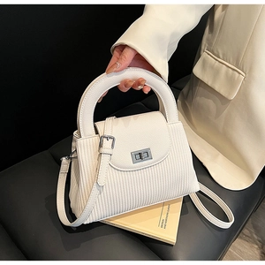 Detail of white quilted texture crossbody bag with silver rotating lock on a book
