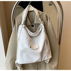 Close-up of white multi-pocket tote bag with silver zippers on a khaki trench coat