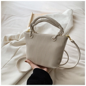 Detail shot of cream pleated bucket bag showing vertical folds and gold metal ring hardware