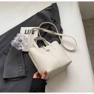 Close-up of white lychee pattern leather bucket bag with snap closure and adjustable strap