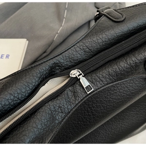 Close-up of silver metal zipper and herringbone lining on a black pebbled leather tote bag