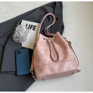 Close-up of pink bucket bag with drawstring, suede texture, and metallic chain details