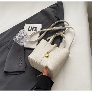 Close-up of white lychee pattern leather bucket bag with golden padlock and detailed texture