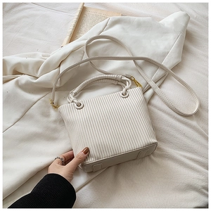 Detail of cream pleated bucket bag with fine vertical stripes and gold metal hardware