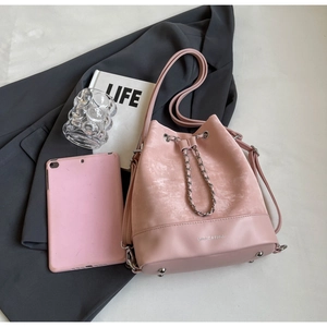 Detail of pink bucket bag with drawstring closure, metal chain, and bottom studs texture