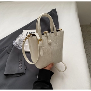 Macro view of cream-colored bucket bag showing lychee grain leather and gold hardware