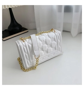Detailed macro of white quilted faux leather texture and gold chain strap on shoulder bag
