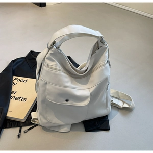 Detail of white leather hobo bag featuring multiple silver zippers and functional pockets