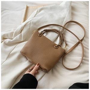 Detail of khaki pleated bucket bag with braided handle and gold hardware on white fabric