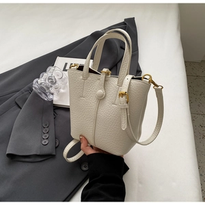 Detailed macro view of cream litchi grain leather bucket bag with gold hardware accents