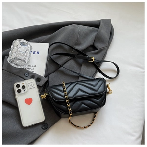 Detail of black quilted leather shoulder bag with gold chain strap on grey blazer