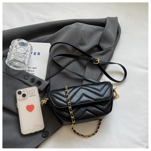 Detail of black chevron quilted crossbody bag with gold chain strap on grey blazer