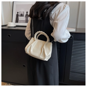 Detail of a creamy white pleated cloud bag with chunky woven handle and silver chain strap