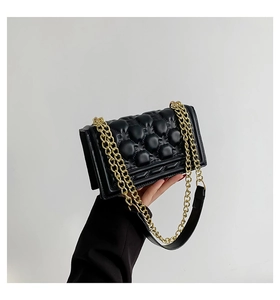 Close-up of black quilted leather square handbag with shiny gold chain strap detail
