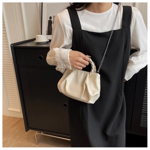Detail of a creamy white pleated cloud bag with woven handle and elegant metal chain strap