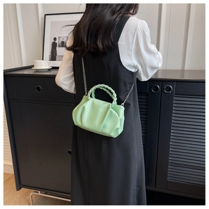 Detail of mint green ruched cloud bag with woven handle and silver chain strap on a model