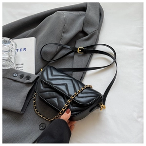Detail of black quilted crossbody bag with golden chain strap and flap closure