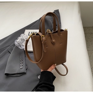 Detail of dark brown pebble leather bucket bag with gold ring handles and adjustable strap
