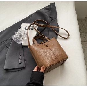 Detailed close-up of a brown litchi pattern leather bucket bag on a blazer and book