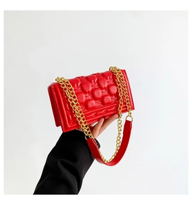 Detail of red quilted square handbag with golden chain strap and padded texture finish