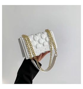 Detailed view of white quilted leather texture and golden metal chain strap on the handbag