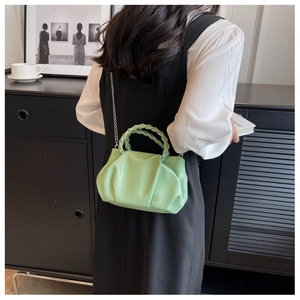 Detailed close-up of light green pleated handbag with woven handle and gold chain strap