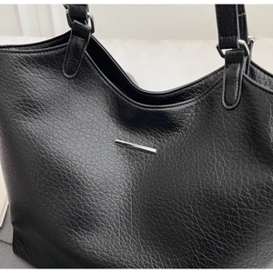 Detailed macro view of black lychee-textured leather tote bag with silver metal buckles
