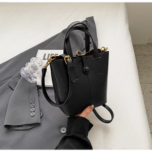 Detail of black pebbled leather bucket bag with gold hardware and long shoulder strap