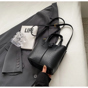 Close-up of black lychee grain leather bucket bag with top handle and sleek buckle detail