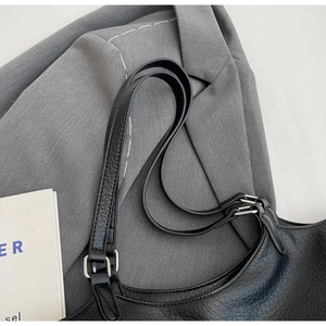 Detail of lychee textured black leather tote bag with silver metal buckles on gray suit