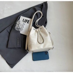 Flat lay of cream bucket bag with drawstring closure and silver chain detail