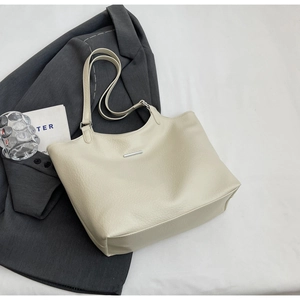 Detail of off-white tote bag with lychee texture and silver metal trim on grey blazer