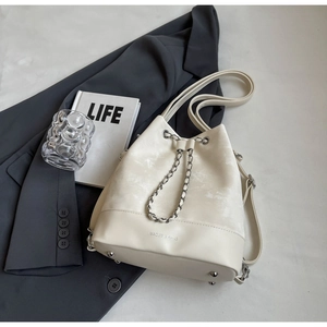 Detail of cream drawstring bucket bag with chain strap and brand logo on soft suede texture