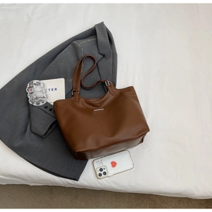 Flat lay of brown pebble leather tote bag on white bedding with a gray blazer jacket