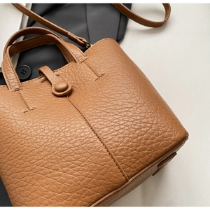 Close-up of brown litchi grain leather texture and button closure on bucket bag