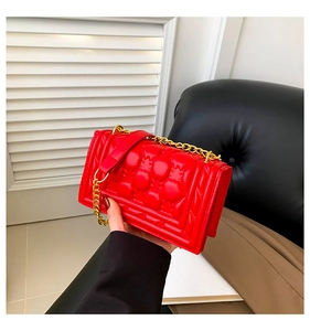 Detailed view of red quilted square handbag with gold chain strap and glossy finish