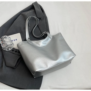 Close-up of silver tote bag with lychee grain texture and metal logo on a grey blazer