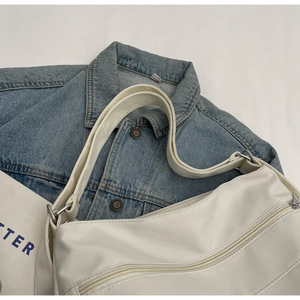 Detail view of white leather shoulder bag with wide strap and silver zipper accents