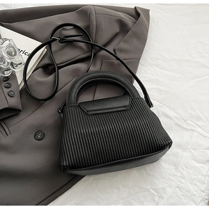 Detail of black pleated texture handbag with smooth leather handle and adjustable strap