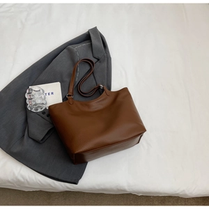 Detail view of brown pebbled leather tote bag with silver hardware on a gray blazer