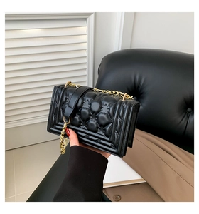 Detail of black quilted shoulder bag with gold chain strap and textured leather finish