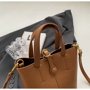 Detail of lychee pattern brown leather bucket bag with golden hardware on a grey blazer