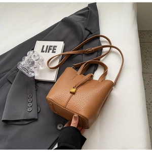 Detail view of brown lychee leather bucket bag with gold lock on grey suit background