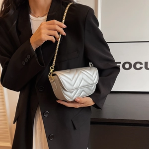 Silver quilted crossbody bag with gold chain strap worn by a model in black blazer