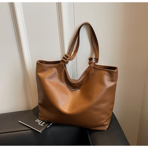Detailed view of the brown lychee-pattern leather texture and metallic bar on the tote bag