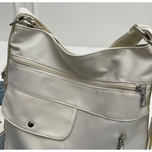 Detailed macro view of white nylon tote bag with multi-zipper pockets and metal buckle