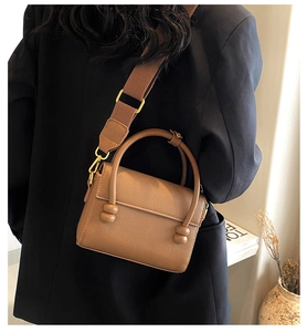 Petit sac carré marron en cuir grainé porté en bandoulière sur une veste noire